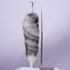 May include: A grey and white faux fur tail keyring with a silver metal ring.