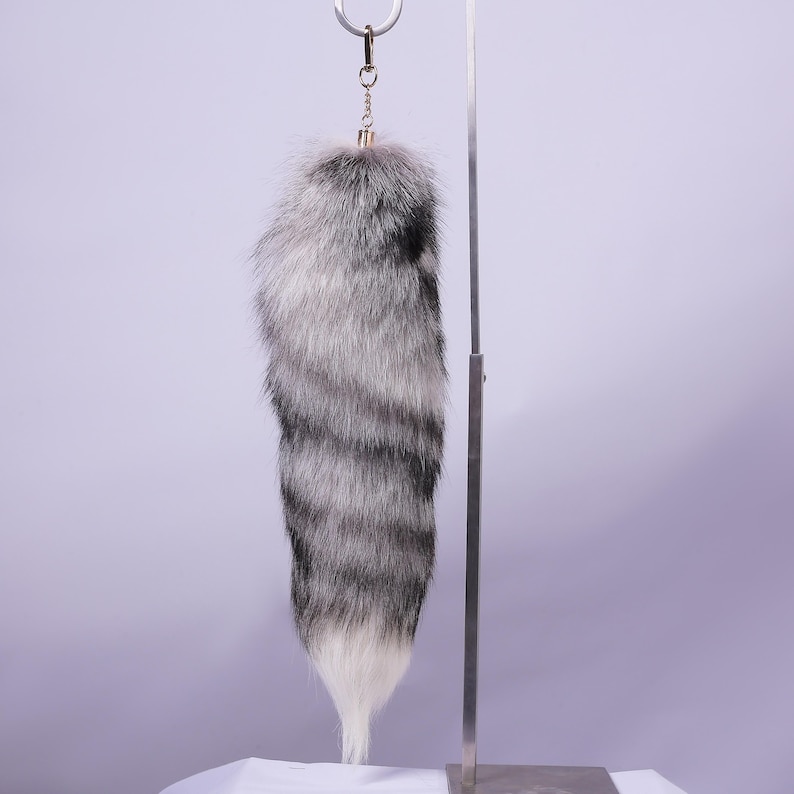 May include: A grey and white faux fur tail keyring with a silver metal ring.