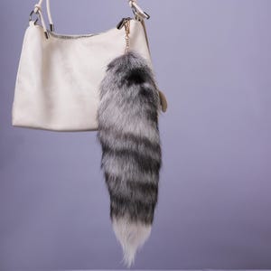 May include: A white faux leather handbag with a silver chain and a fluffy grey and white fox tail keychain.