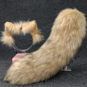 Op de afbeelding: Een set bruine nep bont kattenoren en staart. De oren zijn bevestigd aan een hoofdband en de staart is lang en pluche.