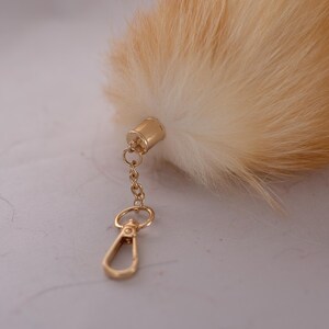 May include: A fluffy, light brown and white fox tail keyring with a gold metal clasp and chain.