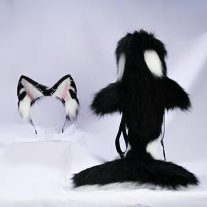 Puede incluir: Un conjunto de disfraz de orca de piel sintética en blanco y negro. El conjunto incluye una pieza de cuerpo tipo mochila con cola y una diadema con detalles de orejas a juego. Las orejas tienen detalles en rosa.