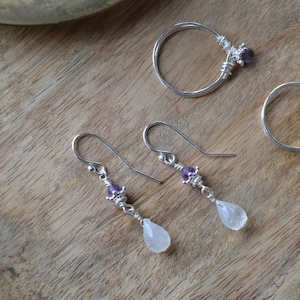 May include: A pair of silver earrings with amethyst and moonstone drops. The earrings are handmade and feature a delicate wire design.