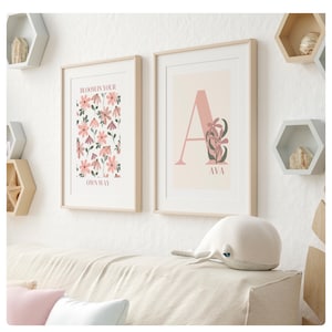 May include: Two framed prints with a floral theme. The left print features a pink and green floral pattern with the text "Bloom in your own way". The right print features a large pink letter "A" with a floral design and the name "Ava" below it.
