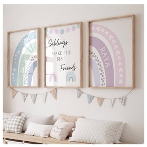May include: Three framed prints with rainbow designs. The center print has the text "Siblings make the best friends" and two rainbow illustrations. The left print has a rainbow with stars and the text "Reuben". The right print has a rainbow with hearts and the text "Raya".
