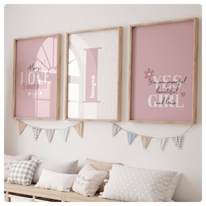 Könnte beinhalten: Drei rosa gerahmte Drucke mit inspirierenden Zitaten und einem Namen. Der erste Druck sagt "Liebe dich immer" mit einem rosa und weißen Sonnenstrahl-Design. Der zweite Druck hat einen großen weißen Buchstaben "I" mit dem Namen "Imogen", der vertikal auf der rechten Seite des Buchstabens geschrieben ist. Der dritte Druck sagt "Ja Mädchen Du bist stark schön und mutig" mit einem rosa Blumendesign.