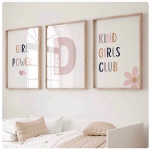 May include: Three framed prints with a pink and white color scheme. The first print says "Girl Power" with a pink heart and a flower. The second print has a large pink letter "D" with the name "Darcy" written inside. The third print says "Kind Girls Club" with a pink flower.