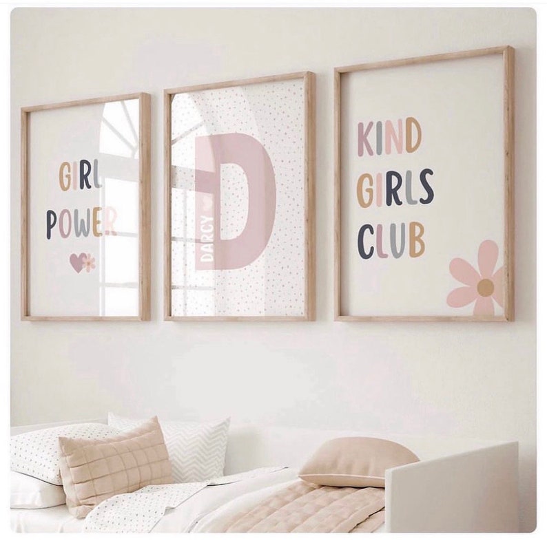 May include: Three framed prints with a pink and white color scheme. The first print says "Girl Power" with a pink heart and a flower. The second print has a large pink letter "D" with the name "Darcy" written inside. The third print says "Kind Girls Club" with a pink flower.