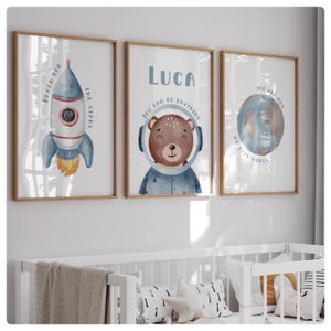 May include: Three framed prints with a space theme. The first print features a blue and white rocket with the text "Reach for the stars". The second print features a brown bear wearing a blue astronaut suit with the text "Luca You can do anything". The third print features a blue and brown planet with the text "You are out of this world".