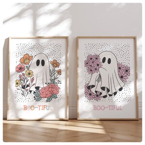 May include: Two framed prints with a white ghost holding flowers. The prints have a white background with black polka dots and the text "BOO-TIFUL" in rainbow colors.