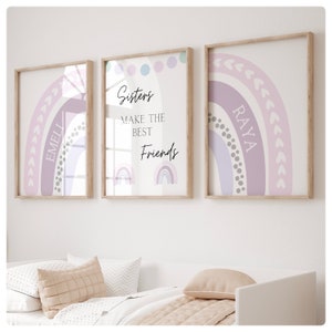 May include: Three framed prints with pastel rainbow designs. The center print has the text "Sisters make the best friends" and two smaller rainbow illustrations. The left print has the name "Emeli" and the right print has the name "Raya".