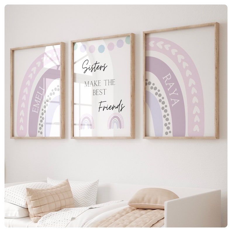 May include: Three framed prints with pastel rainbow designs. The center print has the text "Sisters make the best friends" and two smaller rainbow illustrations. The left print has the name "Emeli" and the right print has the name "Raya".