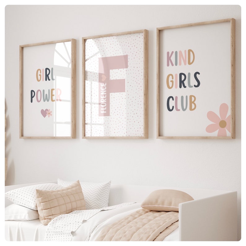 May include: Three framed prints with a pink and white polka dot background. The first print says "Girl Power" in colorful letters with a pink heart and a flower. The second print has a large pink letter "F" with the word "Florence" written vertically beside it. The third print says "Kind Girls Club" in colorful letters with a pink flower.