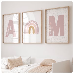 May include: Three framed prints with a pink and white polka dot background. The first print features the letter A in pink with the name Anaiah written vertically. The second print features a rainbow with pink, orange, and yellow stripes. The third print features the letter M in pink with the name Margot written vertically.