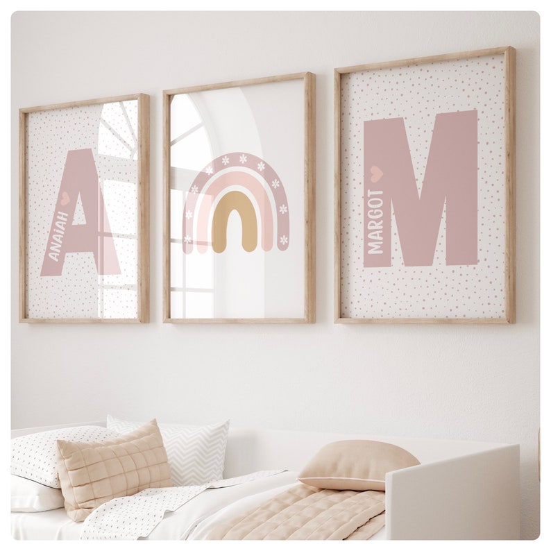 May include: Three framed prints with a pink and white polka dot background. The first print features the letter A in pink with the name Anaiah written vertically. The second print features a rainbow with pink, orange, and yellow stripes. The third print features the letter M in pink with the name Margot written vertically.