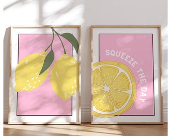 Könnte beinhalten: Zwei gerahmte Drucke mit rosa Hintergrund. Der erste Druck zeigt zwei gelbe Zitronen mit grünen Blättern. Der zweite Druck zeigt eine Zitronenscheibe mit dem Text "Squeeze the Day".