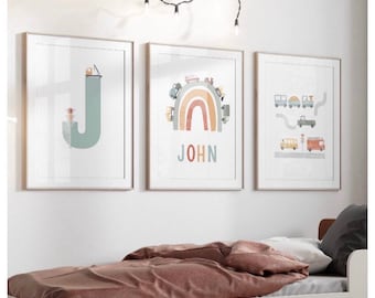May include: Three framed prints with a light wood frame. The left print features a light blue letter J with a small truck on top. The middle print features a rainbow with a light brown, orange, and yellow color scheme. The rainbow has small trucks and cars on top. The text "JOHN" is below the rainbow. The right print features a light blue road with a yellow school bus, a red fire truck, and a gray truck.