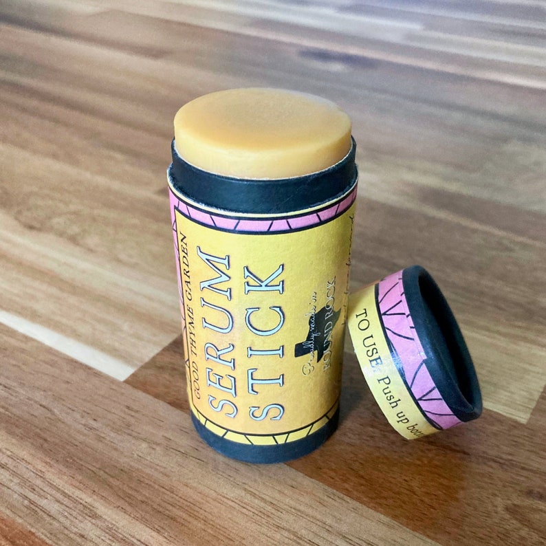 May include: A yellow and black serum stick with a light brown top, and the text "SERUM STICK" in large letters. The packaging also includes the text "GOOD THYME GARDEN" and "TO USE: Push up bottom". The cap is pink and black.