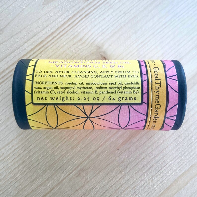 May include: A cylindrical skincare product with a label featuring a geometric floral design in yellow, orange, and pink. The label includes product information, ingredients, and a net weight of 64 grams.
