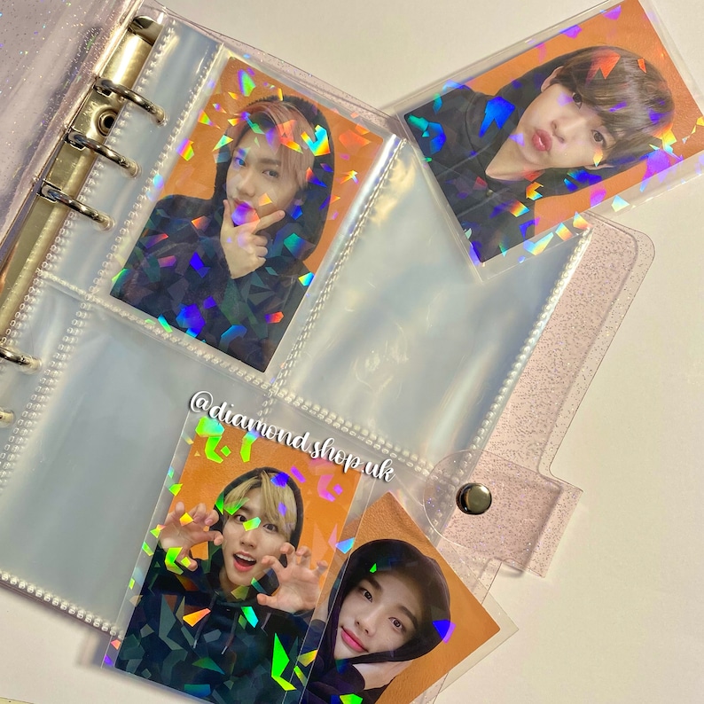 K&ouml;nnte beinhalten: Ein durchsichtiger Plastikordner mit schimmernden, holografischen Fotokartenh&uuml;llen. Die H&uuml;llen enthalten Fotos einer Boyband. Der Text "@diamondshop.uk" ist auf dem Ordner sichtbar.
