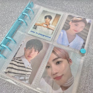 May include: A clear plastic binder with a light blue spine and silver glitter embedded in the plastic. The binder has several clear plastic pockets that hold photo cards of various people. The text "stay in playground" is written on a white card in the binder.