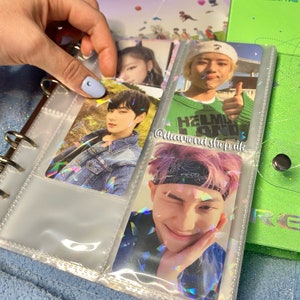 K&ouml;nnte beinhalten: Ein durchsichtiger Plastikordner mit holografischem Finish enth&auml;lt Foto-Karten von verschiedenen K-Pop-Idolen. Der Ordner hat einen Ringmechanismus und ist mit durchsichtigen Plastikh&uuml;llen gef&uuml;llt. Die Foto-Karten zeigen Bilder der Idolen mit verschiedenen Hintergr&uuml;nden und Gesichtsausdr&uuml;cken. Der Text "@diamond.shop.uk" ist auf dem Ordner sichtbar.