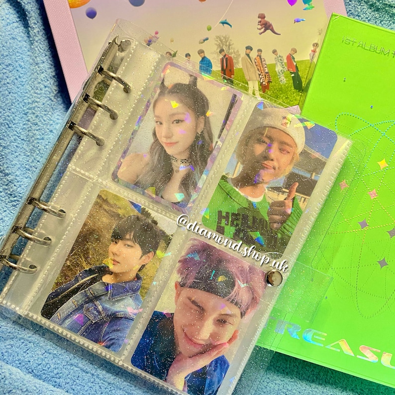 K&ouml;nnte beinhalten: Ein durchsichtiger Plastikordner mit glitzernder Oberfl&auml;che enth&auml;lt Foto-Karten von verschiedenen K-Pop-Idolen. Der Ordner hat einen silbernen Ringmechanismus und ist mit durchsichtigen Plastikh&uuml;llen gef&uuml;llt. Die Foto-Karten zeigen Bilder der Idolen in verschiedenen Posen und Umgebungen. Der Ordner ist ge&ouml;ffnet, um die Foto-Karten zu zeigen, die in Reihen angeordnet sind. Der Ordner liegt auf einer gr&uuml;nen Oberfl&auml;che mit wei&szlig;em Hintergrund.