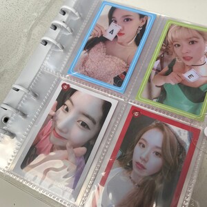 May include: A clear plastic binder with a collection of photo cards featuring a K-pop girl group. The cards are in clear plastic sleeves and feature different members of the group. The cards have a pink and white heart logo with the text "Twice" on them. The cards feature the letters "A" and "E" on them.