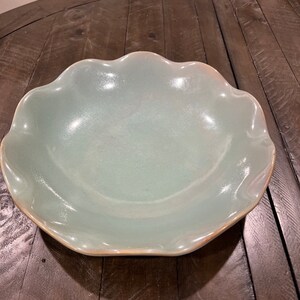 May include: A light blue ceramic serving bowl with a scalloped edge. The bowl has a glossy finish and a light brown rim. This decorative bowl is suitable for serving salads, fruits, or other dishes.