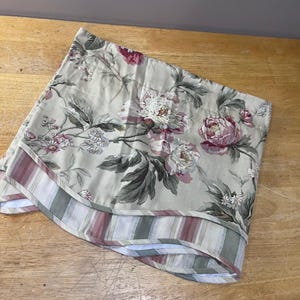 May include: A floral patterned fabric with large pink and white peony blooms and green leaves. The fabric has a beige background and a striped border in shades of red, green, and white.