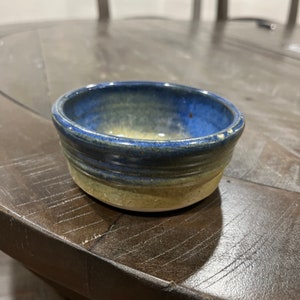 May include: A small, blue and beige ceramic bowl with a rounded rim. The bowl has a glazed finish and is perfect for serving small snacks or dips.