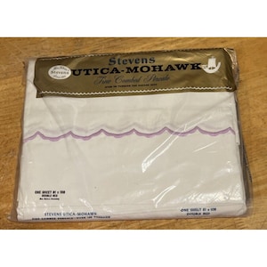 May include: A packaged white double bed sheet with a scalloped purple border. The packaging features the text "Stevens UTICA-MOHAWK Fine Combed Percale" in gold lettering. The sheet measures 81 x 108 inches.