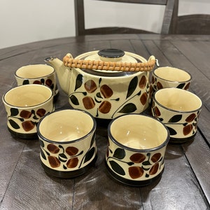 May include: A brown and cream ceramic teapot with a floral design and a woven bamboo handle, along with six matching teacups.