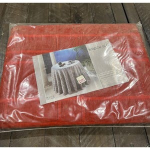 May include: A red rectangular tablecloth, packaged in clear plastic, with a textured surface and a striped pattern. A printed paper insert shows a table setting and the words "WINDOW PAN".