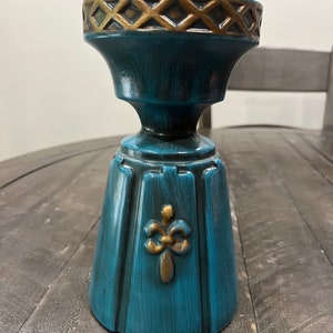 May include: Teal blue ceramic candle holder with a gold trim and a gold fleur-de-lis design.