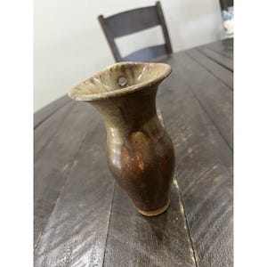 May include: A handcrafted ceramic vase with a unique, organic shape. The vase features a flared top and a narrow base. The color palette includes shades of brown and tan, with a glossy finish. A small hole is visible near the top. This vase is perfect for displaying flowers.