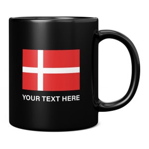 May include: Black ceramic mug with the Danish flag, a red field with a white cross. The mug has a curved handle and the text "YOUR TEXT HERE" printed below the flag. The mug is designed for hot drinks and measures approximately 9.5 cm in height.