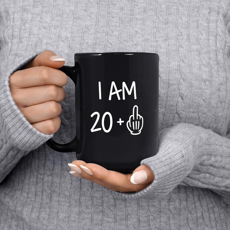 May include: Black coffee mug with white text that reads "I AM 20 +" with a middle finger emoji.