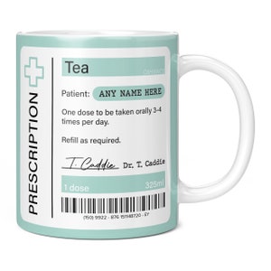 May include: A white ceramic mug with a light blue design that looks like a prescription label. The mug says "Tea" and has a cross symbol. The text on the label says "Patient: ANY NAME HERE" and "One dose to be taken orally 3-4 times per day. Refill as required." The label also has a signature that says "T. Caddie" and "Dr. T. Caddie". The mug has a barcode and the text "1 dose" and "325ml".