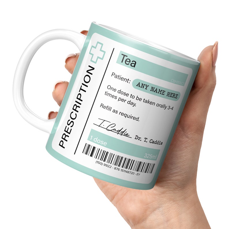 May include: A light blue ceramic mug with a white handle. The mug has a prescription label that reads "Tea" and includes the text "Patient: ANY NAME HERE" and "One dose to be taken orally 3-4 times per day. Refill as required." The label also includes a handwritten signature that reads "T. Caddie" and the text "Dr. T. Caddie". The mug has a barcode and the text "1 dose" and "325ml".