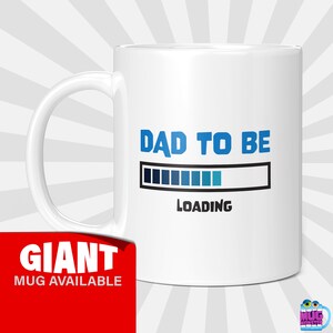 Peut inclure: Mug en céramique blanche avec l'inscription "DAD TO BE" en bleu, un graphique de barre de chargement et le mot "LOADING" en dessous. Une bannière rouge indique "GIANT MUG AVAILABLE".