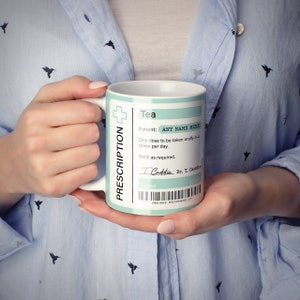 May include: White ceramic mug with a blue and green prescription label that reads "Tea" and "Patient: ANY NAME HERE". The label also includes instructions for taking the tea, a signature, and a barcode.