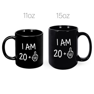 May include: Two black coffee mugs with white text that reads "I AM 20 +" with a middle finger emoji. The mug on the left is 11 oz and the mug on the right is 15 oz.