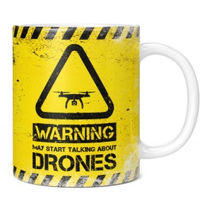 May include: Yellow mug with a black warning sign that says "WARNING MAY START TALKING ABOUT DRONES". The sign has a black triangle with a drone inside.