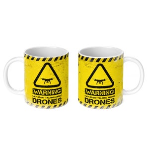 May include: Two white ceramic mugs with a yellow and black warning sign design. The sign features a drone icon and the text "WARNING MAY START TALKING ABOUT DRONES".