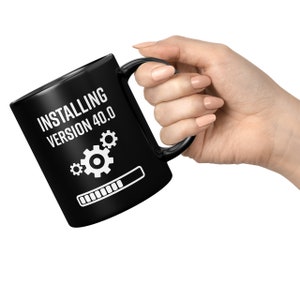 May include: Black coffee mug with white text that reads "Installing Version 4.0.0" with a progress bar and three gears.