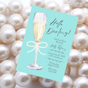 Könnte beinhalten: Eine hellblaue Einladungskarte mit dem Text "Hello Darling!" und Veranstaltungsdetails, die ein Aquarell-Champagnerglas mit einer Perlen-Schleife zeigt. Die Karte ist von weißen Perlen umgeben.
