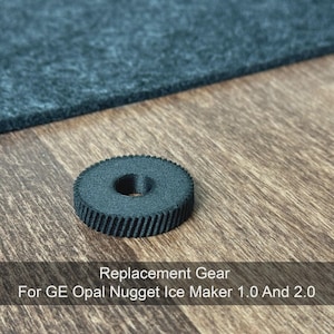 May include: A dark gray replacement gear for a GE Opal Nugget Ice Maker 1.0 and 2.0. The gear is circular with a central hole and ridged edges. The text "Replacement Gear For GE Opal Nugget Ice Maker 1.0 And 2.0" is displayed below the gear.