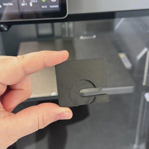 May include: A black, square 3D-printed object with a circular design and a slot, held in front of a 3D printer. The printer's screen displays text: "6 hours on the clock. Let's make another legendary print!"