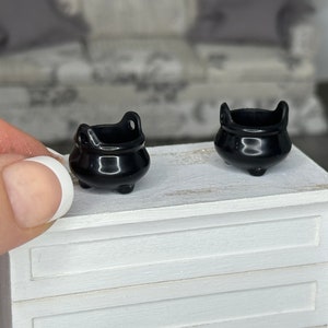 May include: Two small black cauldron shaped pots on a white wooden surface.